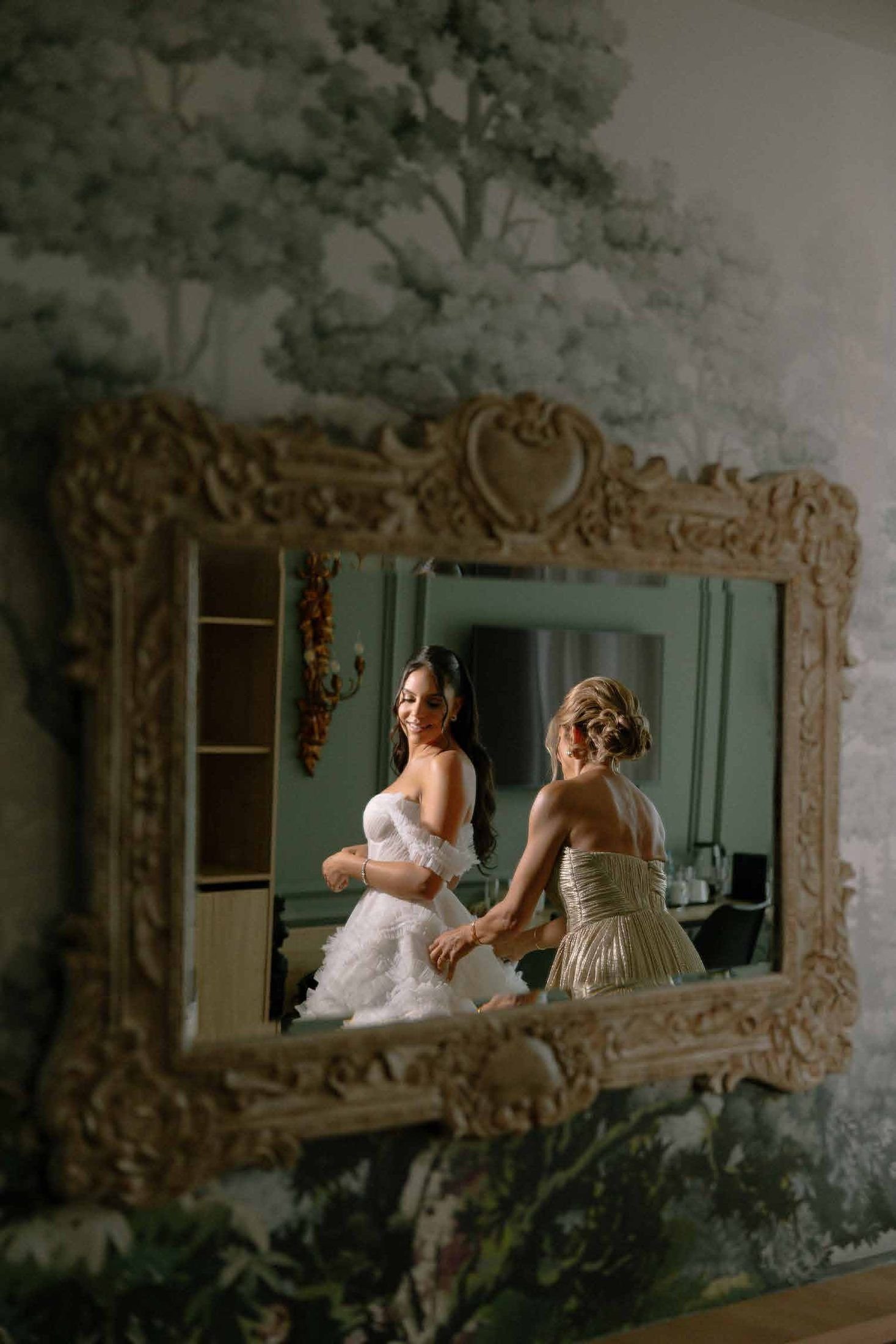 Bride's reflection in an ornate mirror before a botanical mural