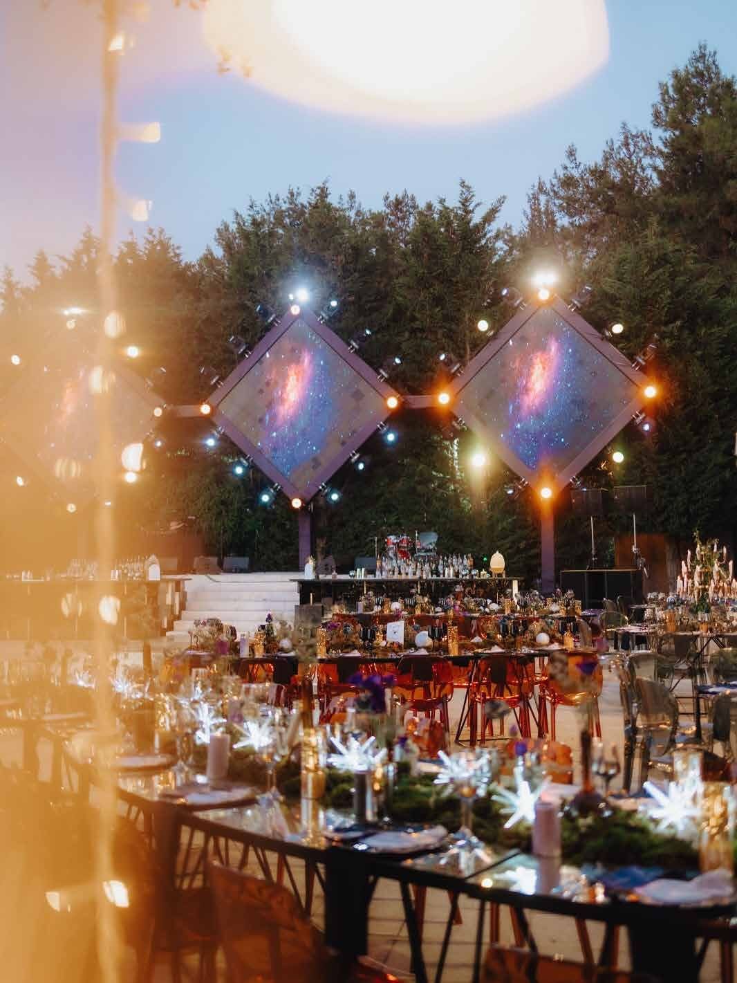 Long table set outdoors at dusk beneath strings of lanterns